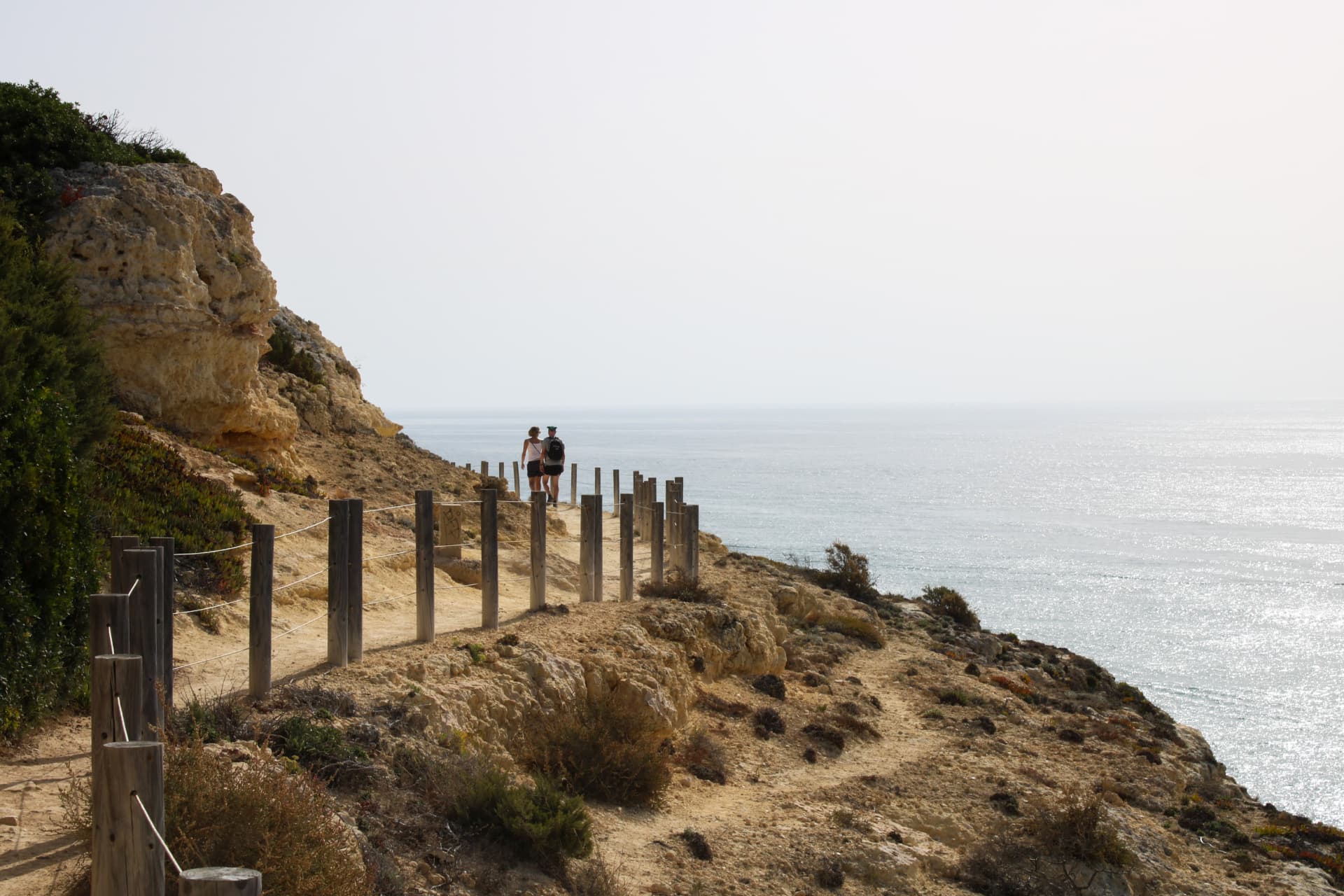 Camino costero del Algarve recorrido por dos figuras humanas junto al paisaje rocoso.